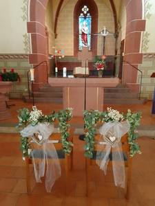 Zwei blumengeschmückte Stühle für das Brautpaar stehen vor dem Altar
